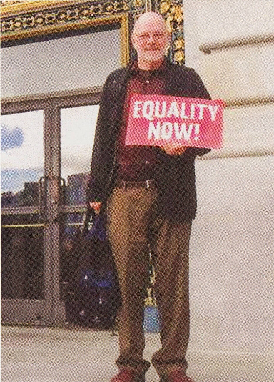 Milt Ford holds a red sign that says "equality now!"